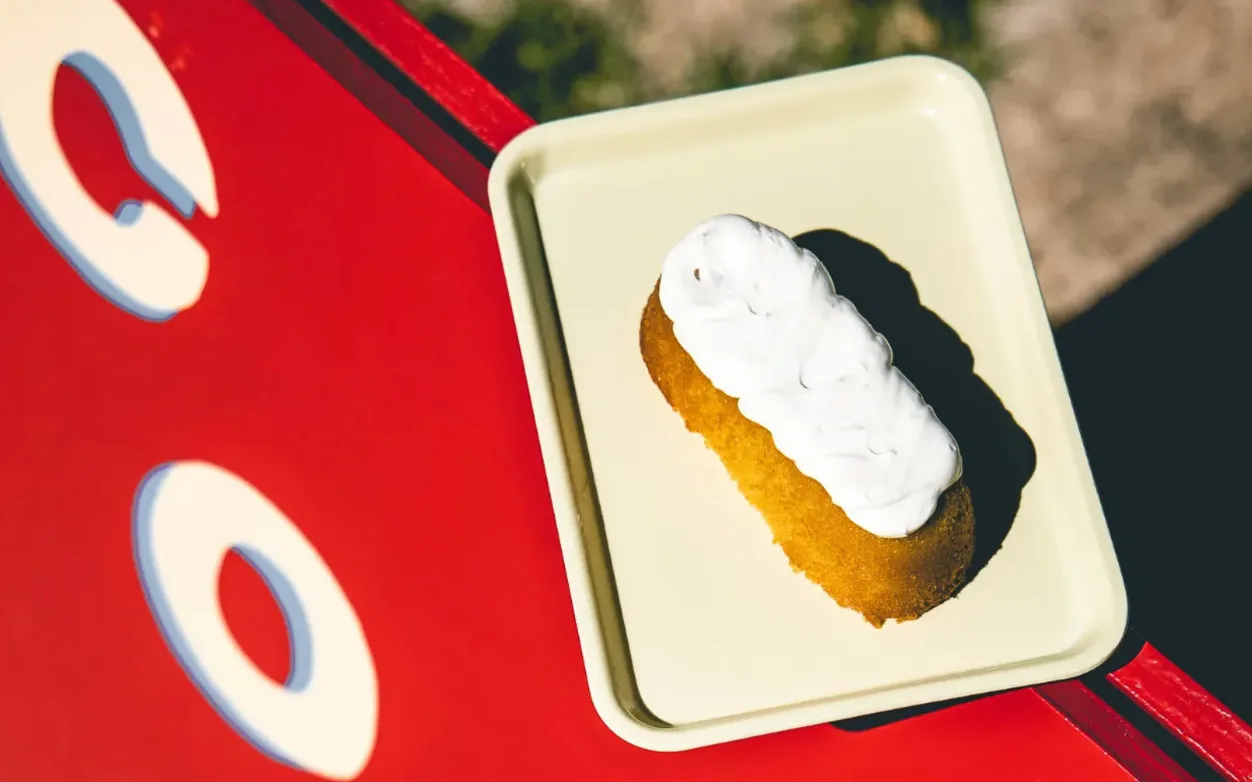 A pastry under a thick layer of white frosting on a pale yellow enamel tray, set on Mercado Sin Nombre’s red coffee cart.