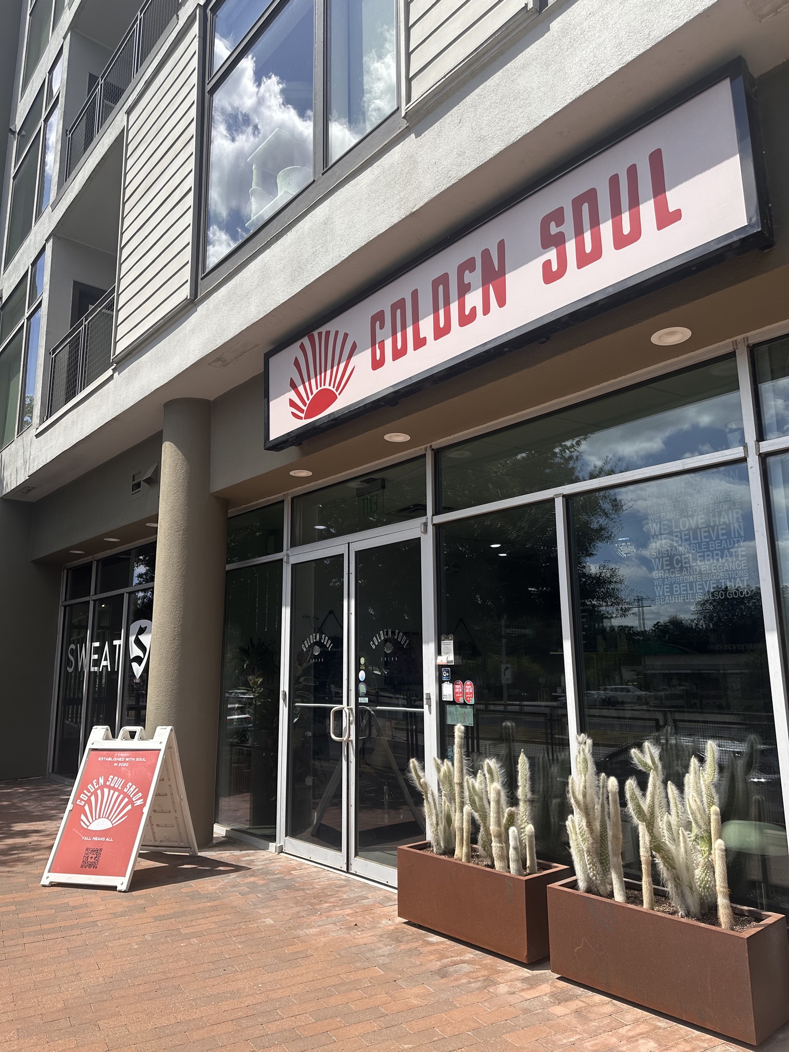 The Golden Soul storefront on South Lamar, a rising-sun logo on the sign and a sandwich board reading y’all means all by the door.