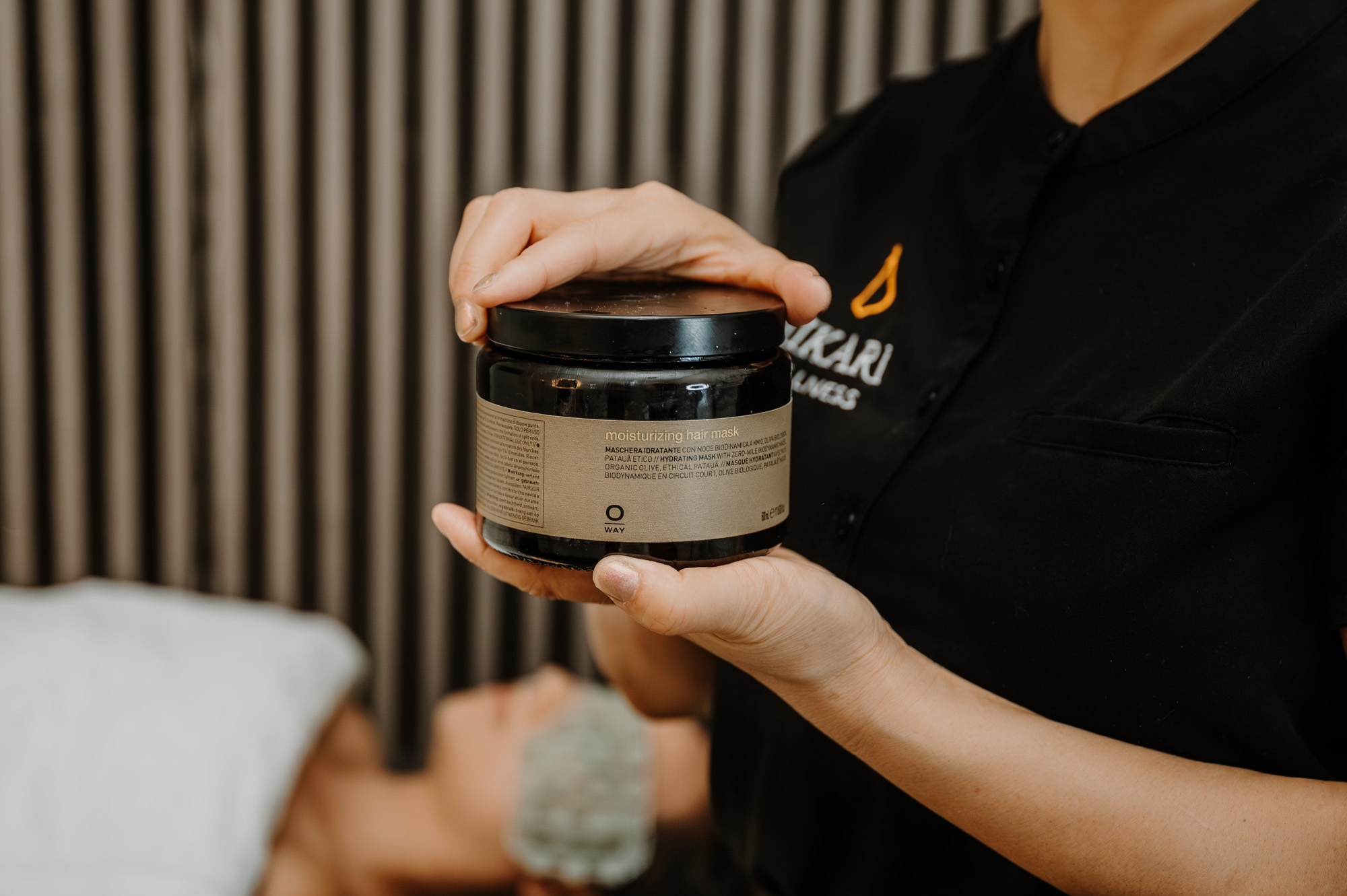 A Hikari Head Spa practitioner holding a jar of Oway moisturizing hair mask in the treatment room.